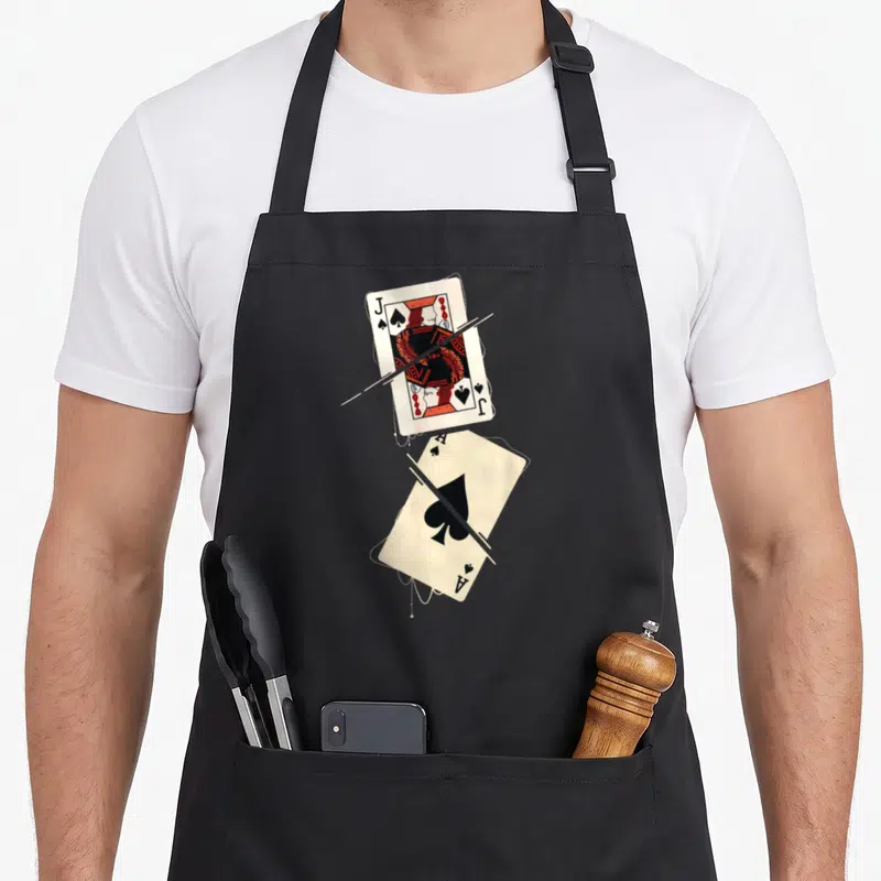 Tablier de cuisine noir avec un Jack et un As de Pique illustrés en style vintage et coupés par des traits blancs.