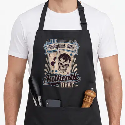 Tablier de cuisine noir avec illustration vintage d'un crâne sur une carte As et le texte The Original 50s Authentic Beat en bleu et noir.