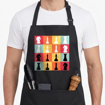 Tablier de cuisine noir avec un motif de pièces d'échecs sur fond de carrés colorés rouge orange et turquoise.