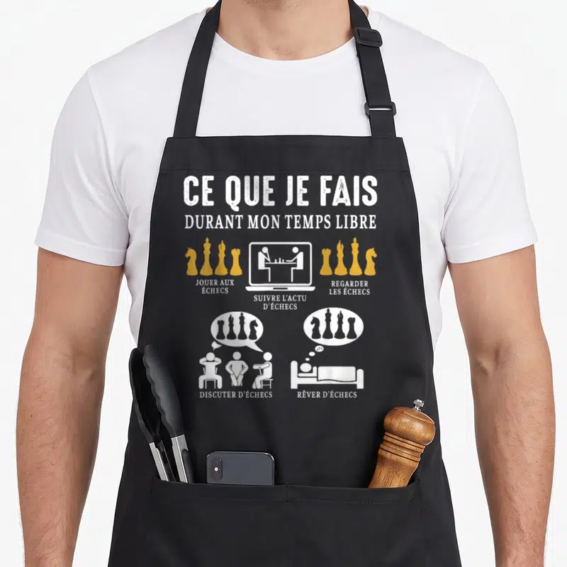 Tablier de cuisine noir avec texte blanc et pièces d'échecs dorées illustrant les passions du joueur.