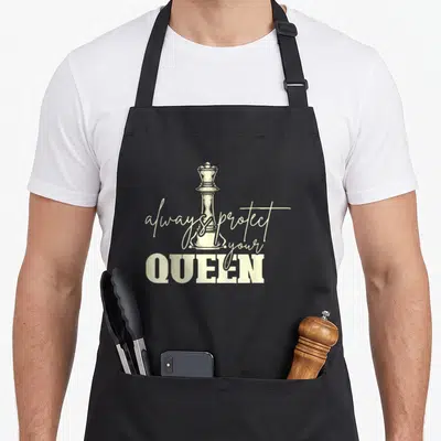 Tablier de cuisine noir avec illustration d'une pièce d'échecs et texte always protect your queen en typographie mixte.