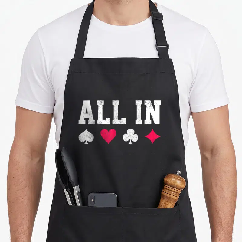 Tablier de cuisine noir avec l'inscription ALL IN et les symboles pique, cœur, trèfle et carreau en blanc et rose vif.