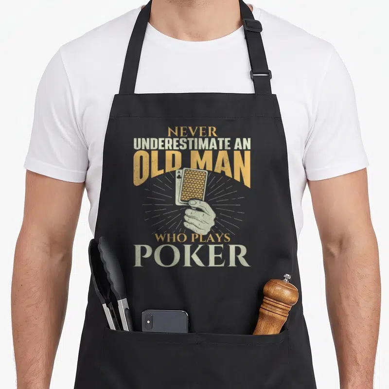 Tablier de cuisine noir avec une main tenant un as de trèfle et le texte Ne sous-estimez jamais un vieil homme qui joue au poker