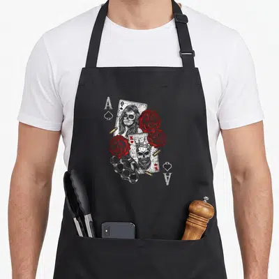 Tablier de cuisine noir avec reine et roi squelette, roses rouges, brassards et cartes à jouer As de pique.
