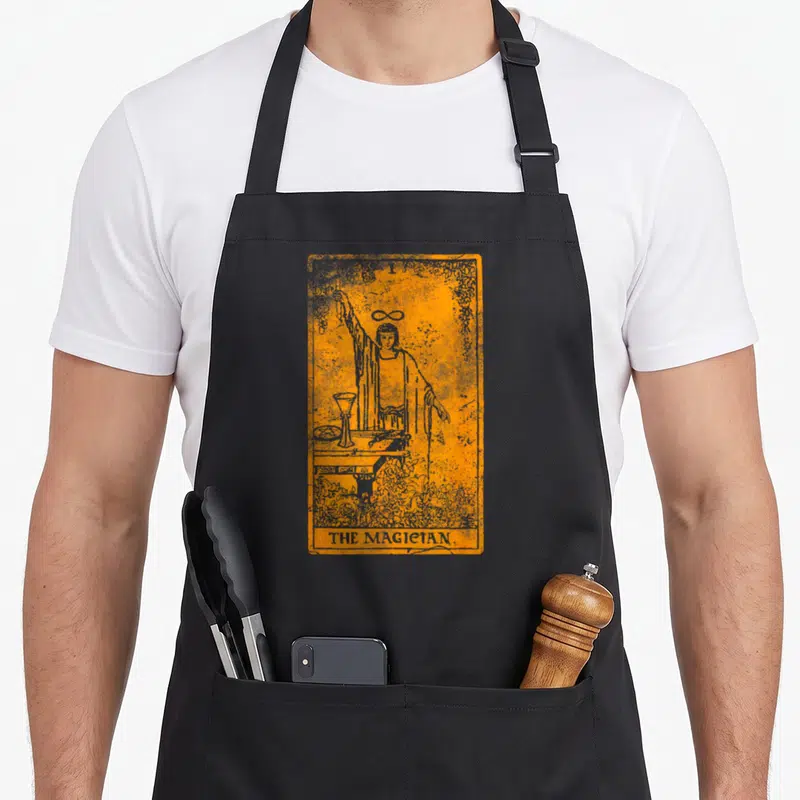 Tablier de cuisine noir avec illustration orange et grise d'une carte de tarot vintage représentant le Magicien.