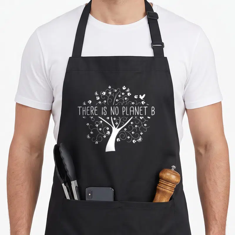 Tablier de cuisine noir avec un arbre blanc stylisé et l'inscription There Is No Planet B au centre des branches.