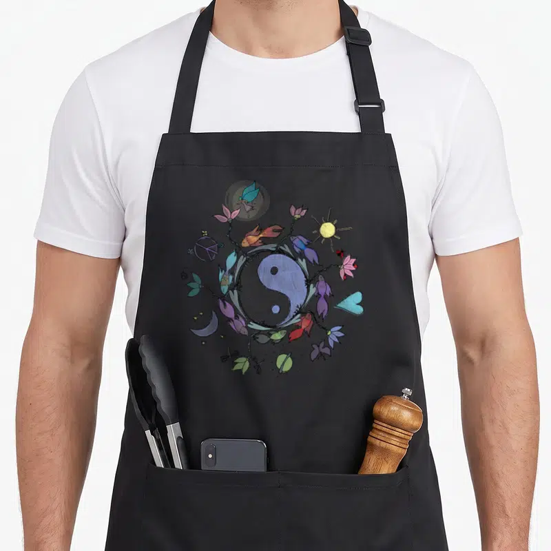 Tablier de cuisine noir avec un grand Ying Yang entouré de poissons colorés, fleurs, soleil et symbole de paix.