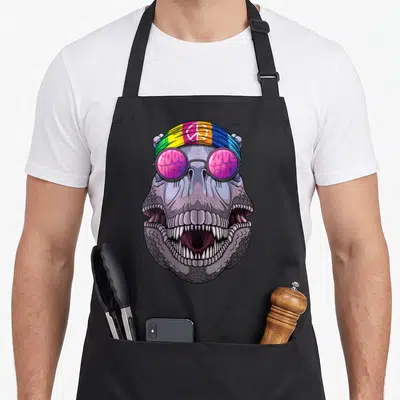 Tablier de cuisine noir avec un dinosaure T-Rex portant un bandeau coloré et des lunettes roses à motifs textuels.
