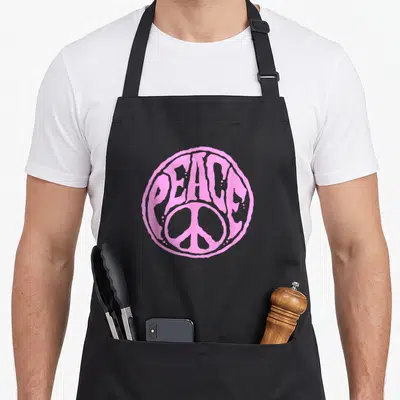 Tablier de cuisine noir avec un grand logo rose en forme de signe de la paix et du mot PEACE imprimé au centre.