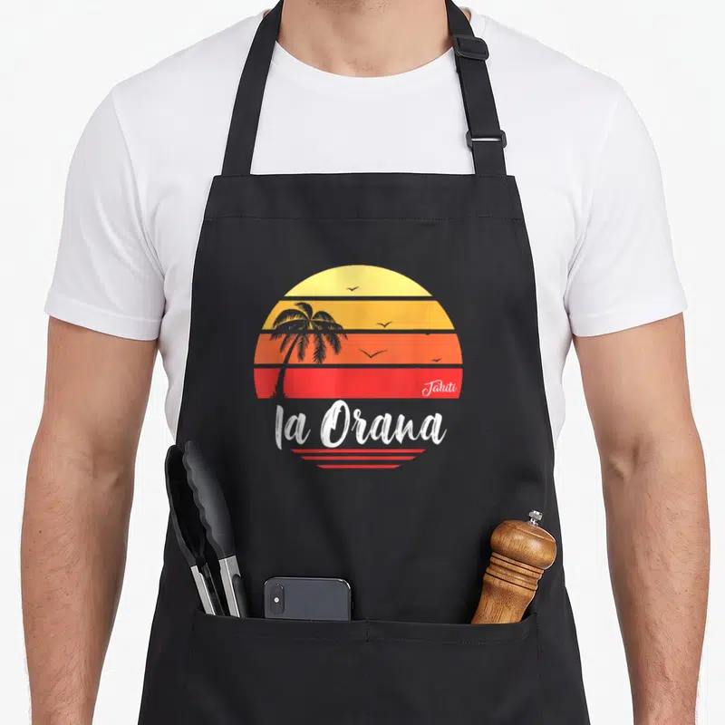 Tablier de cuisine noir avec un soleil tahitien rayé, une palme et le texte la Orana en blanc.