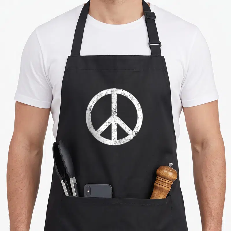 Tablier de cuisine noir avec grand symbole de la paix blanc style vintage et texturé au centre.