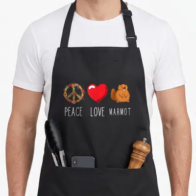 Tablier de cuisine noir avec un symbole de paix floral, un cœur rouge et une marmotte souriante sous les mots Peace Love Marmot.