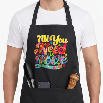 Tablier de cuisine noir avec l'inscription All You Need Is Love en lettres colorées et motifs floraux hippie.