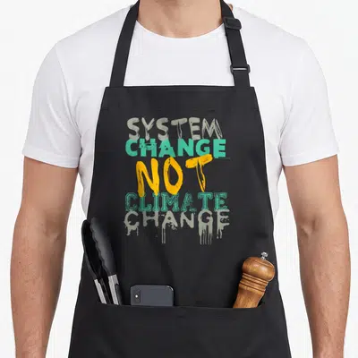 Tablier de cuisine noir avec inscription System Change Not Climate Change en lettres vertes et jaunes style graffiti.