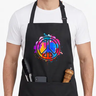 Tablier de cuisine noir avec un grand signe de paix aux éclats de peinture tie dye multicolores sur fond gris.