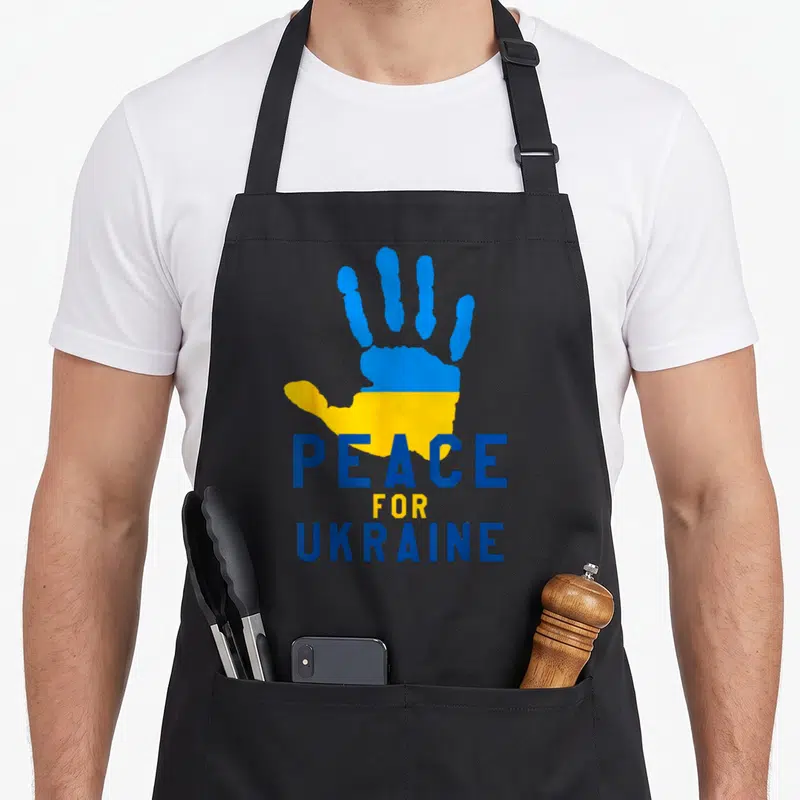 Tablier de cuisine noir avec une main bleue et jaune et le texte Peace for Ukraine imprimé en lettres capitales.