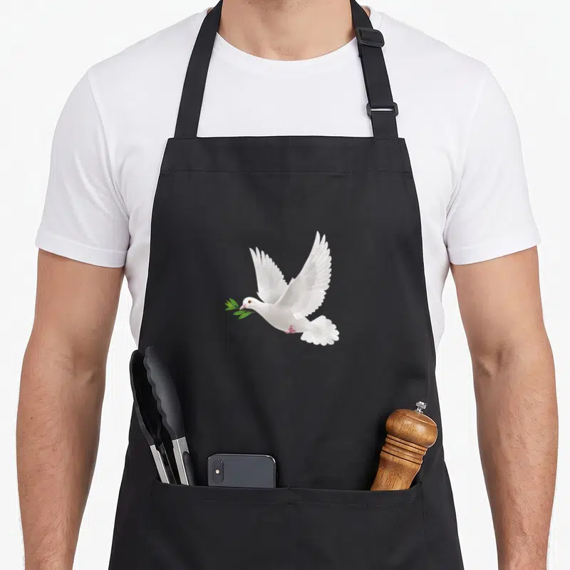 Tablier de cuisine noir avec colombe blanche en vol tenant une branche verte dans son bec.