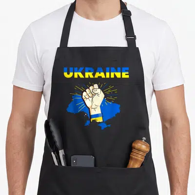 Tablier de cuisine noir avec un poing levé sur une carte bleue et l'inscription Ukraine PAIX en lettres bicolores.