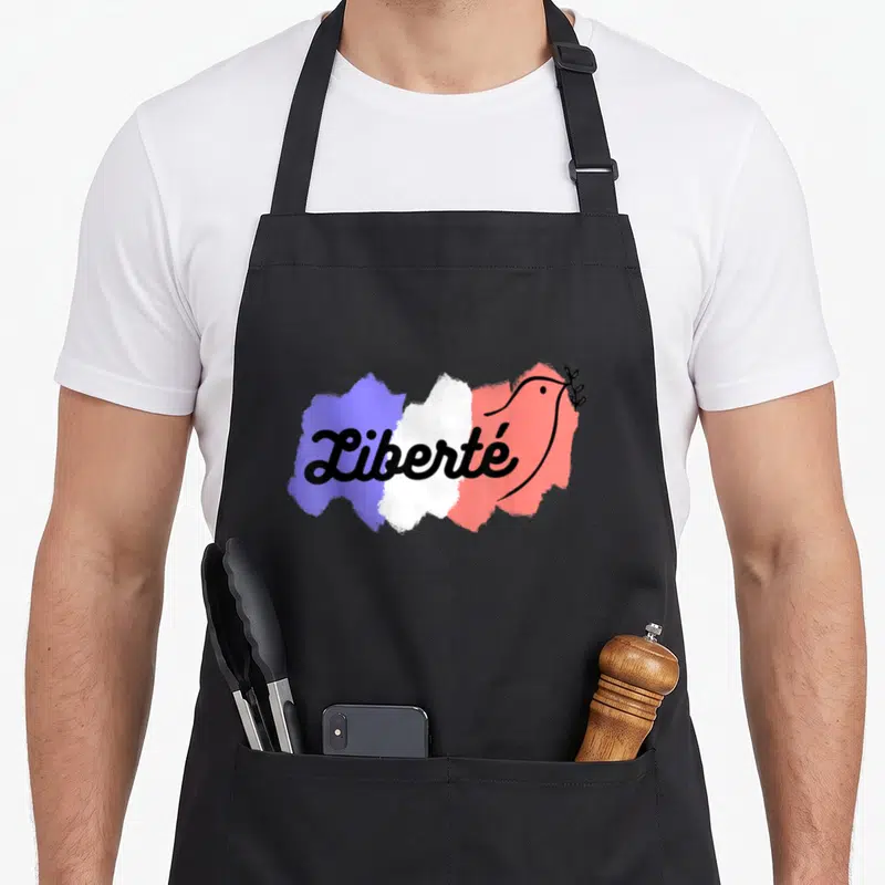 Tablier de cuisine noir avec une colombe stylisée sur un fond aux couleurs bleu blanc rouge et le mot Liberté écrit en noir.