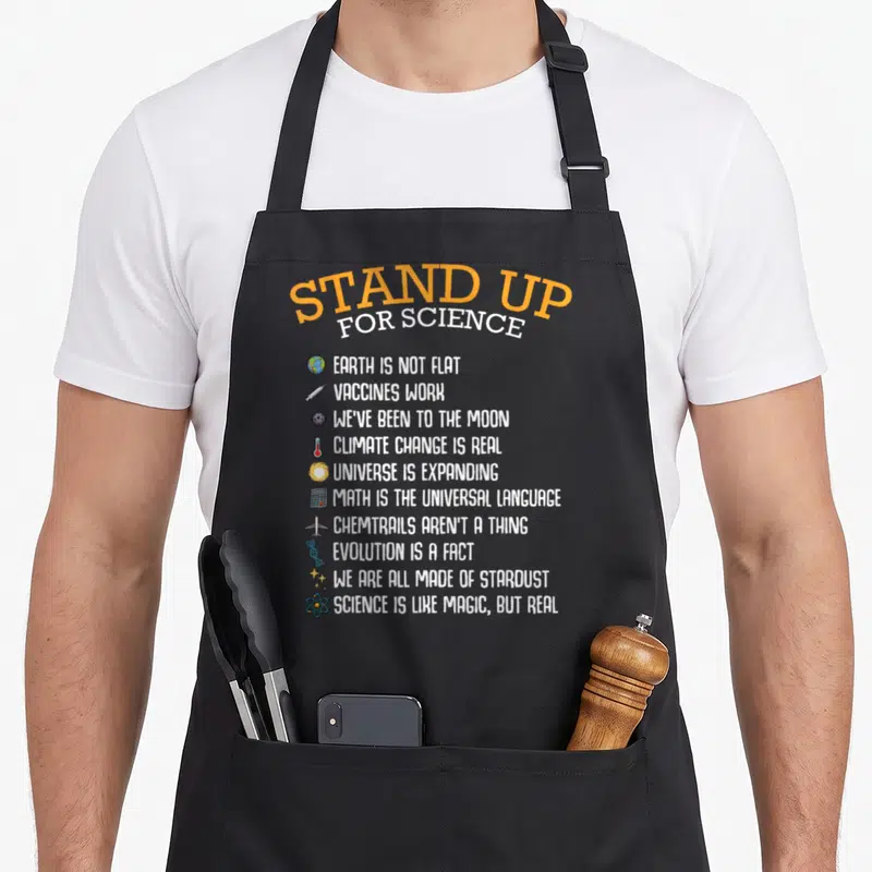 Tablier de cuisine noir avec texte Stand Up For Science et listes de faits scientifiques illustrés par de petits icônes colorées.