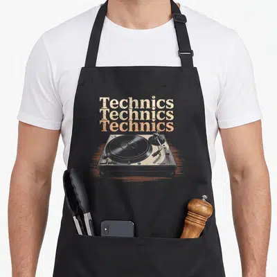 Tablier de cuisine noir avec illustration d'un turntable vintage et texte Technics en lettres délavées beige et orange.