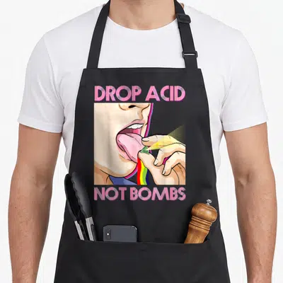 Tablier de cuisine noir avec illustration pop art montrant une bouche et le texte Drop Acid Not Bombs en rose strié.