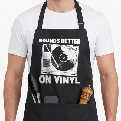 Tablier de cuisine noir orné d'une illustration blanche représentant une platine vinyle et le texte Sounds Better On Vinyl.