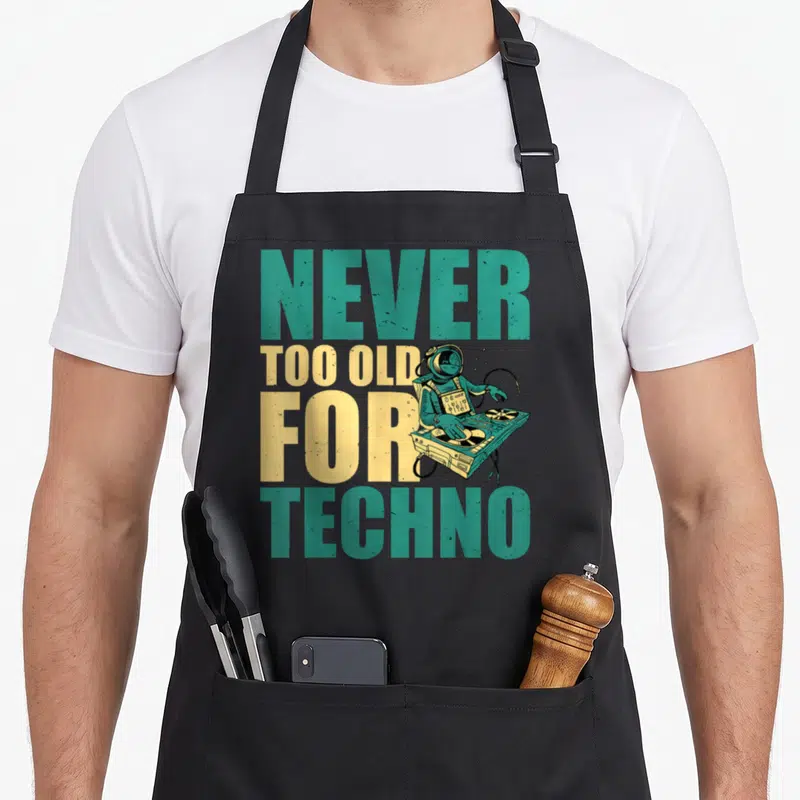 Tablier de cuisine noir avec un astronaute DJ et le texte Jamais trop vieux pour Techno en lettres colorées.