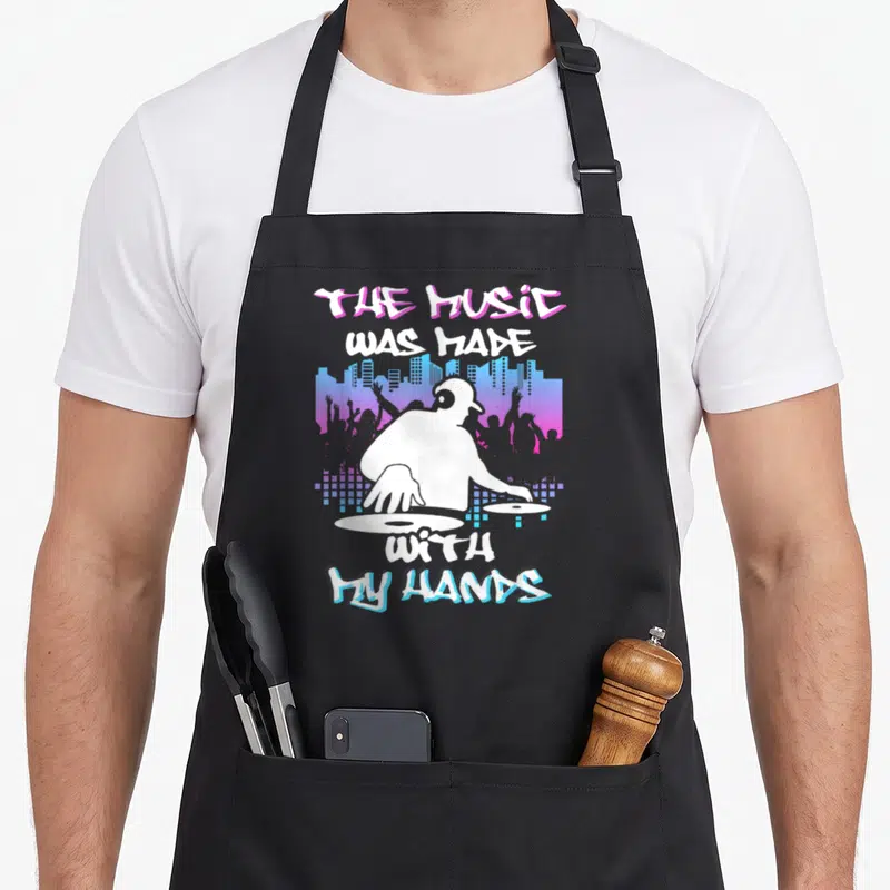 Tablier de cuisine noir avec illustration d'un DJ blanc et le texte The Music Was Made With My Hands.
