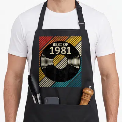 Tablier de cuisine noir avec illustration de disque vinyle noir et texte Best of 1981 sur fond de rayures diagonales multicolores.