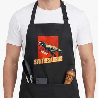 Tablier de cuisine noir avec illustration d'un dinosaure tenant un synthétiseur rouge sur fond texturé.