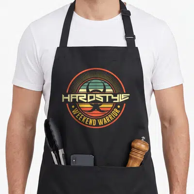 Tablier de cuisine noir avec logo circulaire Hardstyle Weekend Warrior aux couleurs orange et jaune sur fond gris uni.