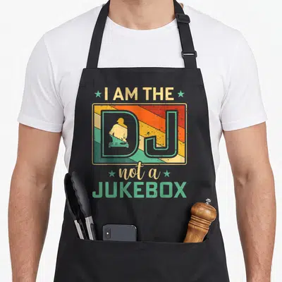 Tablier de cuisine noir avec design vintage I Am The DJ Not A Jukebox et silhouette de DJ sur fond rayé coloré.
