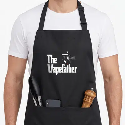 Tablier de cuisine noir avec une silhouette blanche fumant et le texte The Vapefather imprimé au centre.