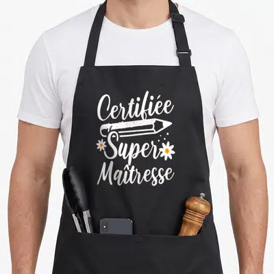 Tablier de cuisine noir avec texte Certifiée Super Maîtresse, crayon blanc et deux petites fleurs jaunes.