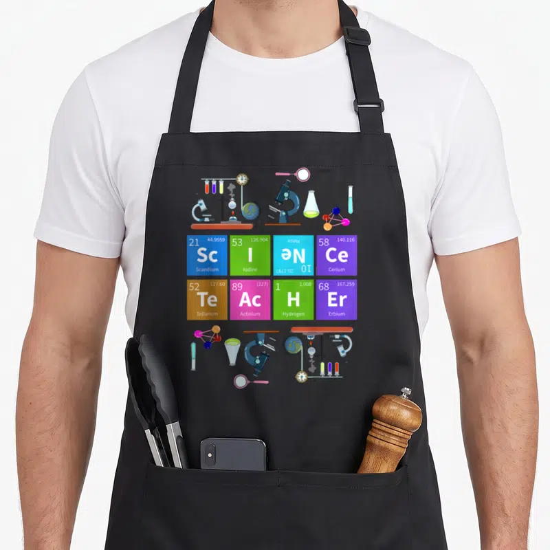 Tablier de cuisine noir avec un tableau périodique coloré, des microscopes et des flacons de laboratoire stylisés.