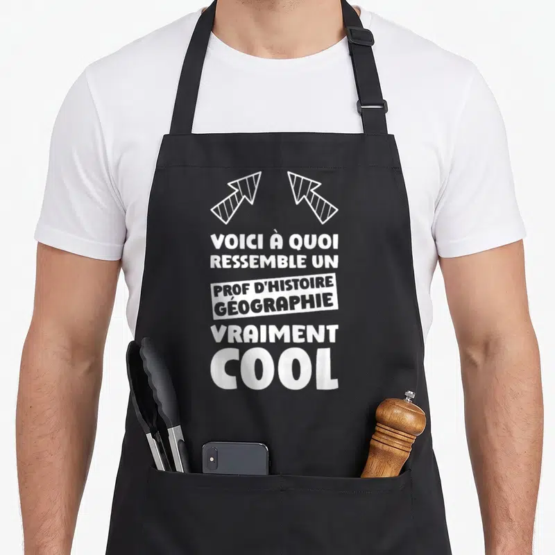 Tablier de cuisine noir avec texte blanc voici à quoi ressemble un prof d'histoire géographie vraiment cool et deux flèches stylisées en haut.
