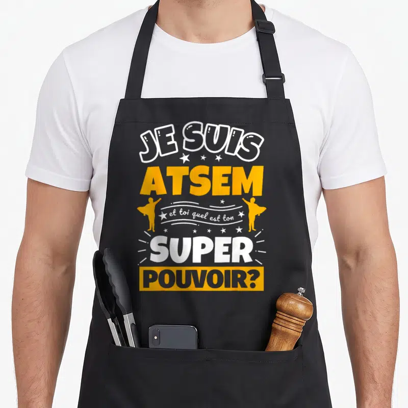 Tablier de cuisine noir avec inscription Je suis ATSEM et toi quel est ton super pouvoir en blanc et orange.