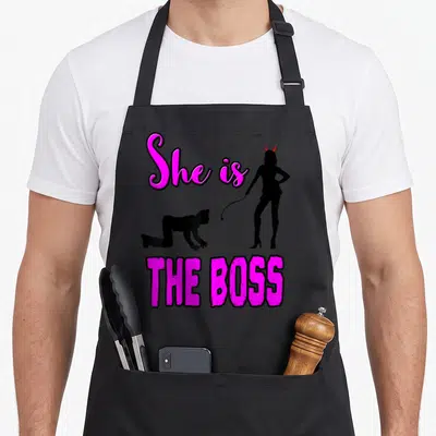 Tablier de cuisine noir avec silhouette maîtresse diable et texte She is The Boss en rose vif.