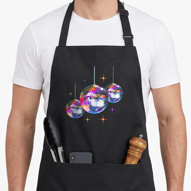 Tablier de cuisine noir avec trois boules disco multicolores suspendues et des étoiles scintillantes aux couleurs vives.
