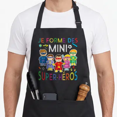 Tablier de cuisine noir avec cinq enfants super-héros et le texte Je forme des mini super-héros en lettres multicolores.