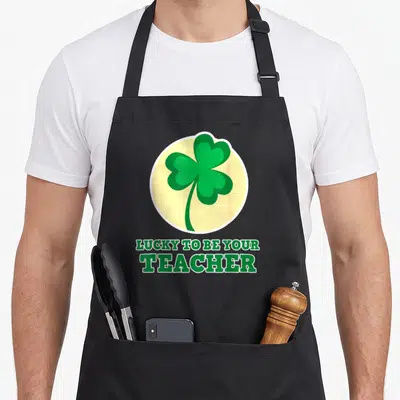 Tablier de cuisine noir avec un trèfle à quatre feuilles vert et le texte Lucky to be your teacher en bas.