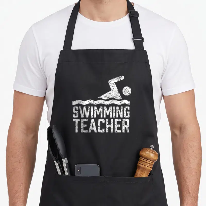 Tablier de cuisine noir avec illustration blanche d'un nageur et le texte Swimming Teacher en typographie usée.