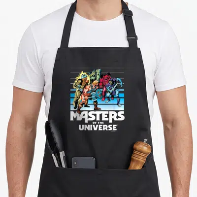 Tablier de cuisine noir avec une illustration colorée des Maîtres de l'univers et le logo blanc en bas.