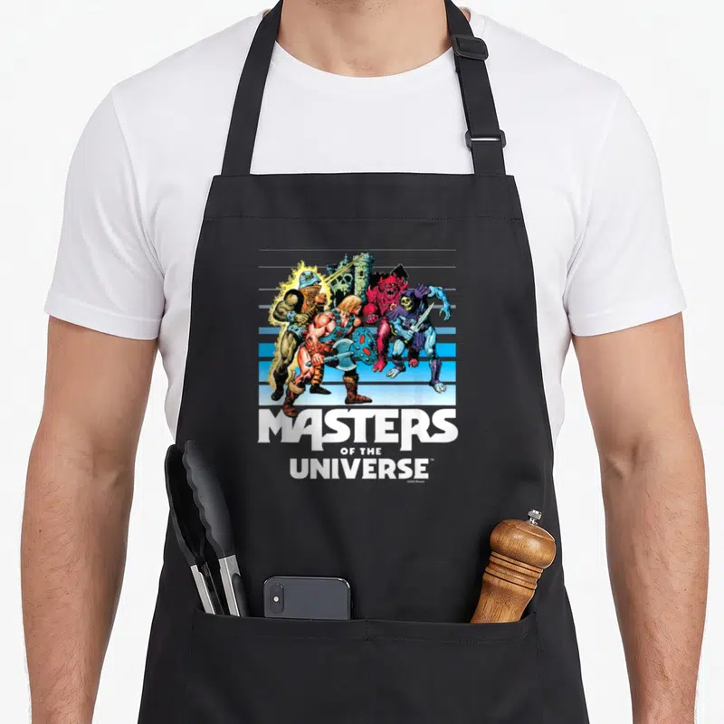 Tablier de cuisine noir avec une illustration colorée des Maîtres de l'univers et le logo blanc en bas.