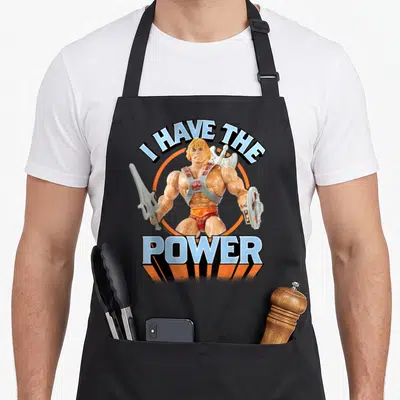 Tablier de cuisine noir avec illustration d'un guerrier blond brandissant une épée et un disque sous le texte I HAVE THE POWER.