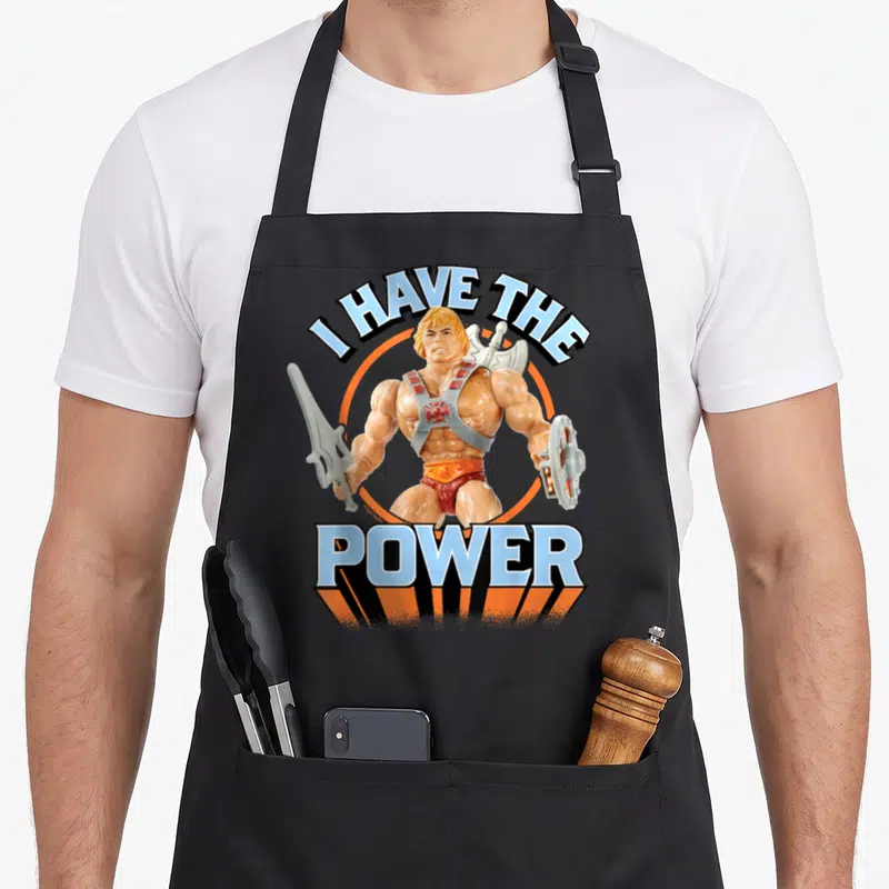 Tablier de cuisine noir avec illustration d'un guerrier blond brandissant une épée et un disque sous le texte I HAVE THE POWER.
