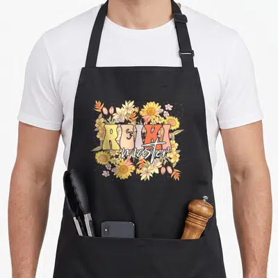 Tablier de cuisine noir avec motif floral Reiki master et fleurs sauvages colorées au centre.