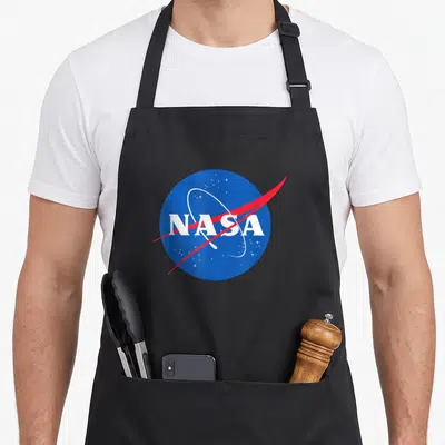 Tablier de cuisine noir avec un emblème circulaire bleu portant l'inscription NASA en lettres blanches et une ligne rouge diagonale.