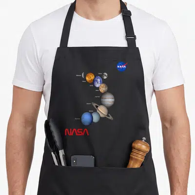 Tablier de cuisine noir avec illustration des planètes du système solaire et logos NASA en haut à droite et en bas.